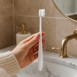 Close-up of a white ultra-soft pregnancy toothbrush held in a woman’s hand in a warm, premium bathroom setting.